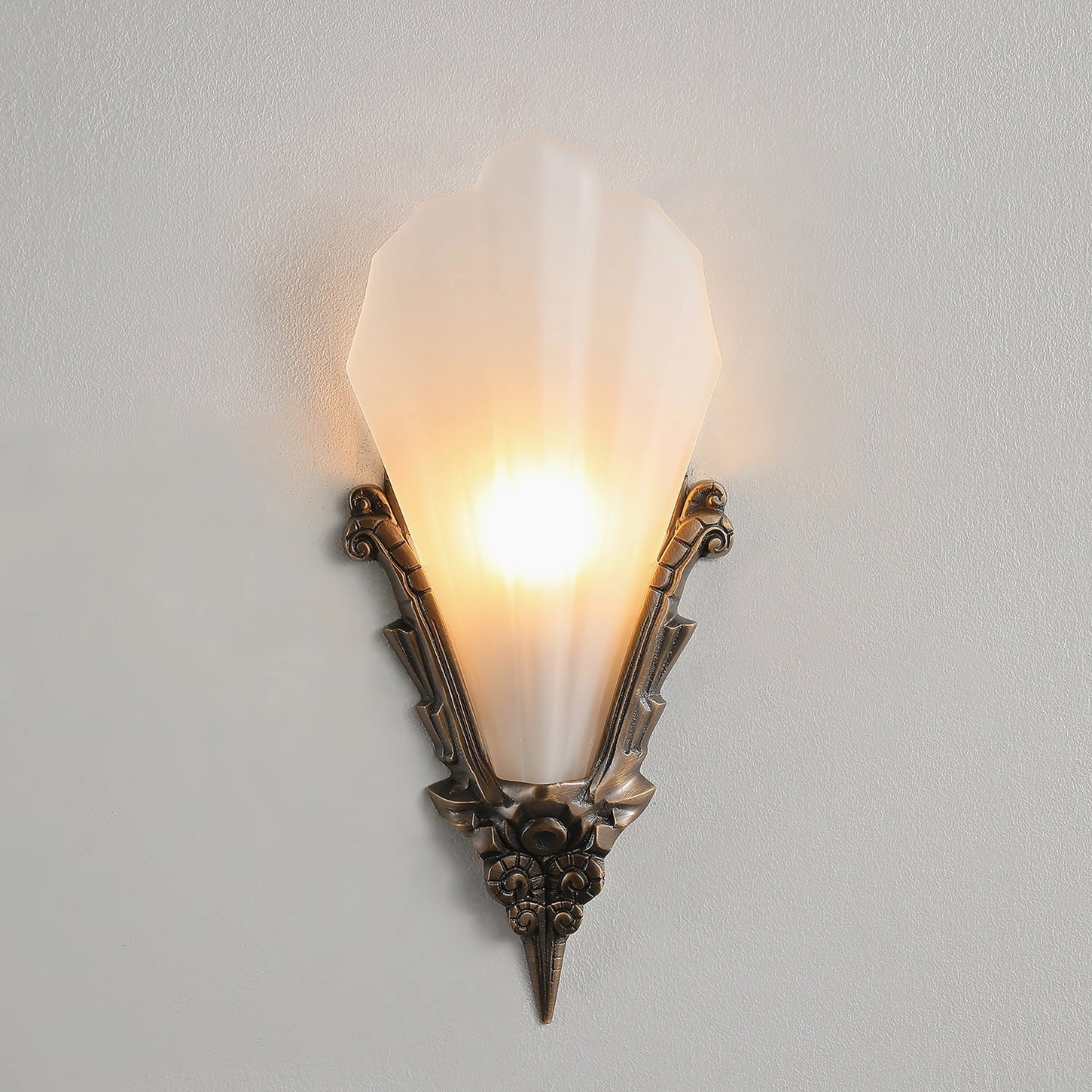 Close-up view of Claridge sconce showing carved bronze hardware and flared frosted glass shade with warm light