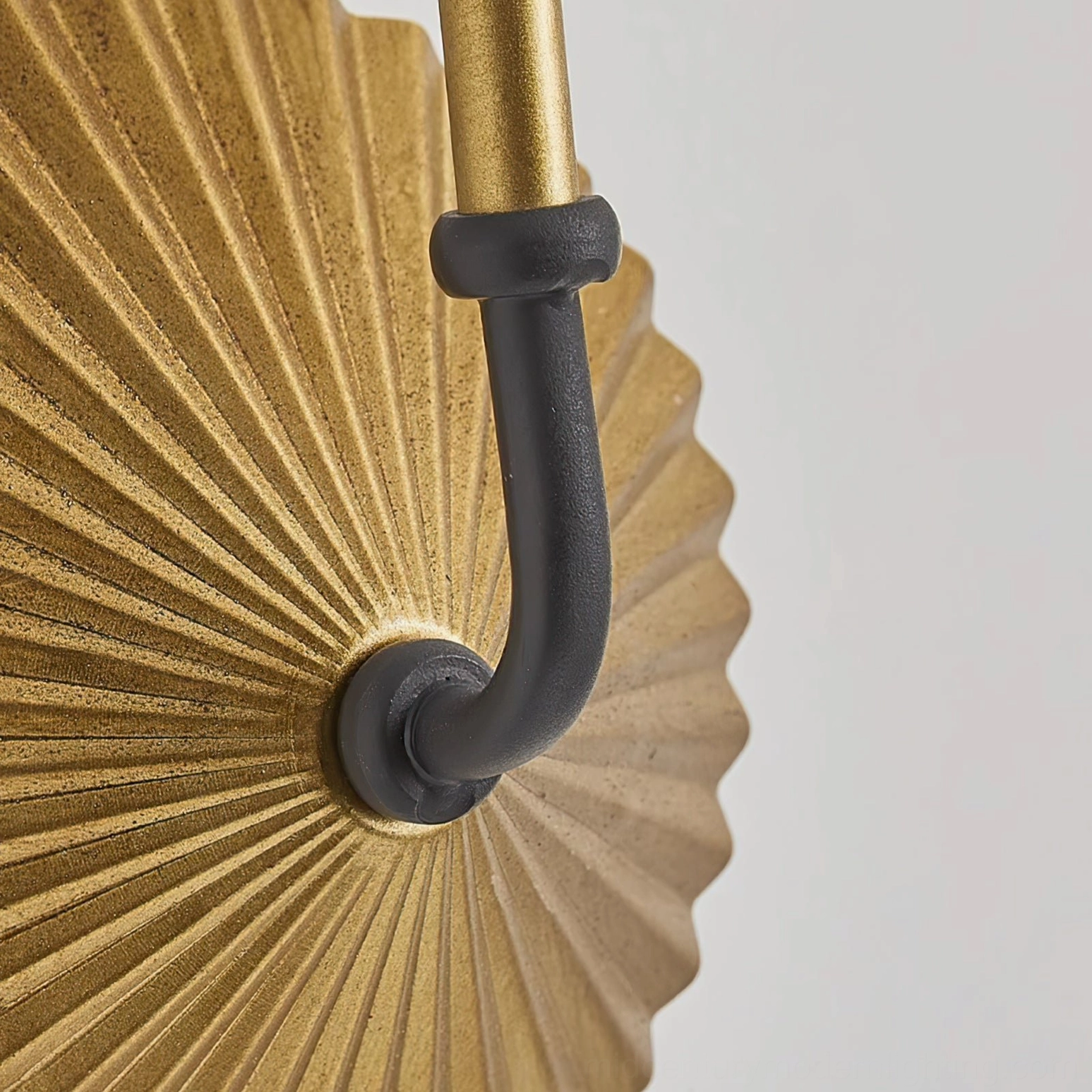 Side profile detail of Clove wall lamp radial pleated gold metal construction and matte black connecting hardware, sculptural accent