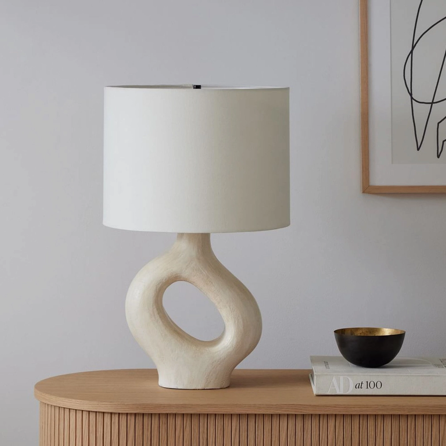 Compact beige Sauce table lamp on wooden fluted sideboard with decorative book and black bowl styling