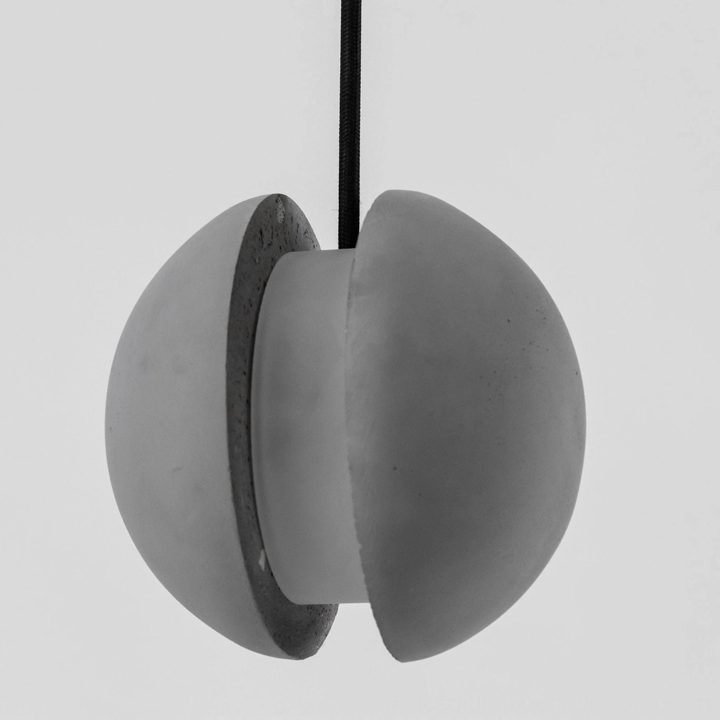 Close-up of split hemispherical concrete pendant lamp showing matte grey texture and exposed interior surface