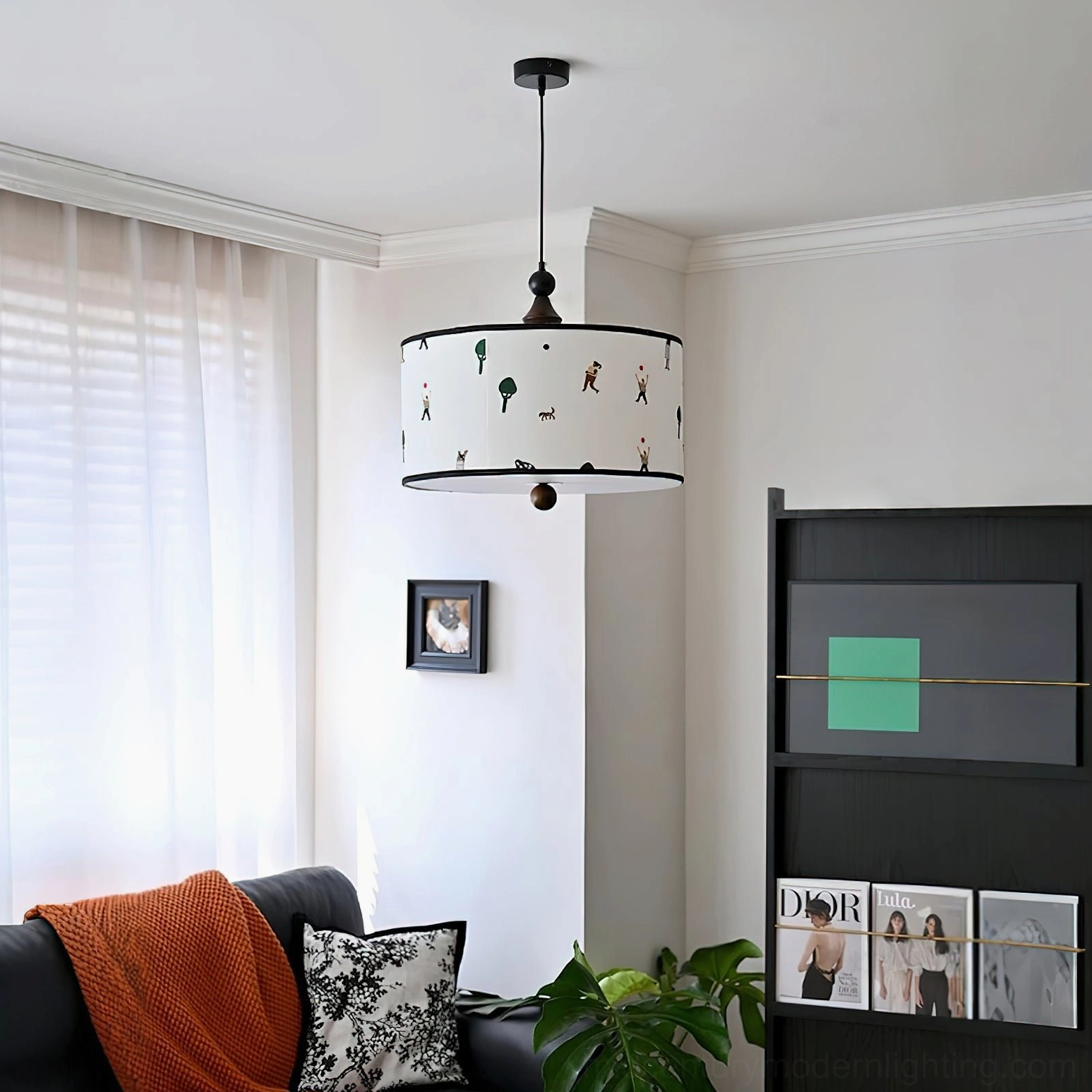 Drum pendant fixture with consistent cartoon print hanging in modern living room with sofa and bookshelf, oblique overhead angle