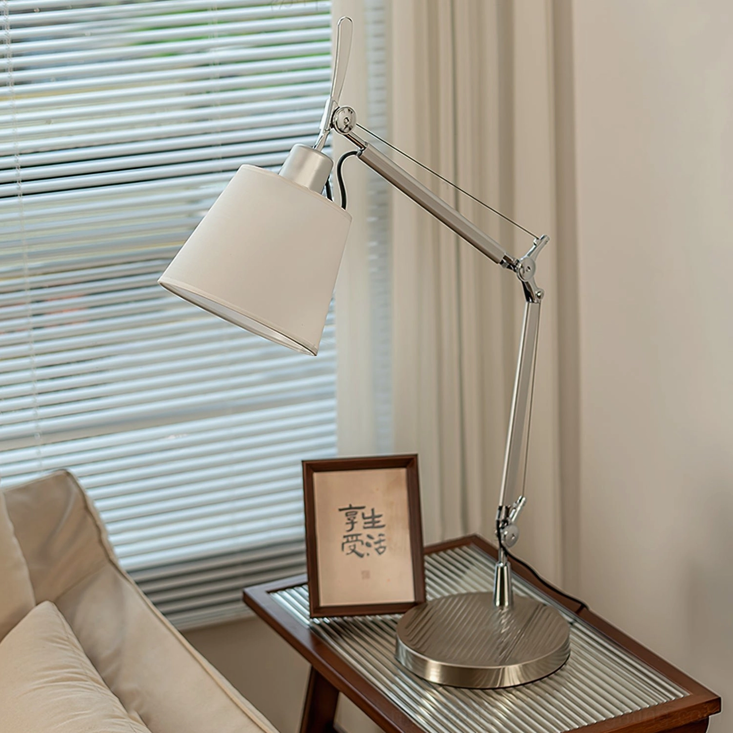Minimalist adjustable lamp on wooden side table in residential interior, showing silver metal frame and fabric shade design