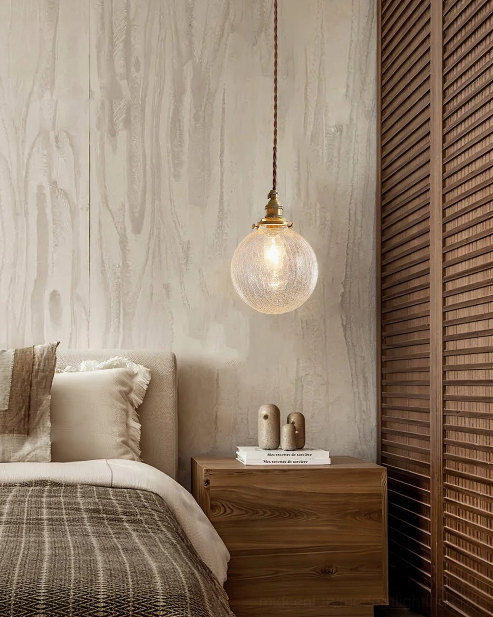 Single crackle glass pendant light in cozy master bedroom above wooden nightstand with neutral bedding and minimalist design