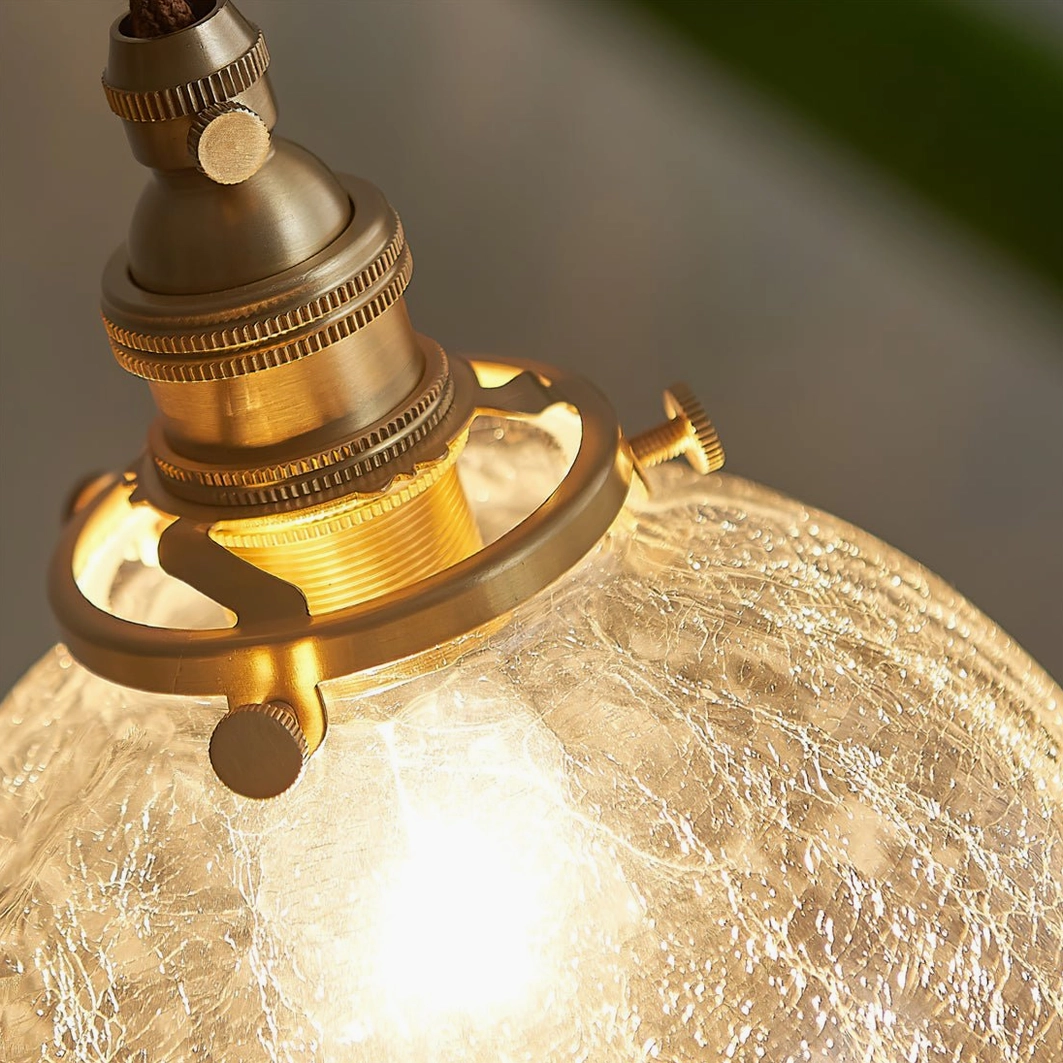 Extreme close-up of crackle glass pendant showing brass adjustable knobs and illuminated fractured glass surface detail