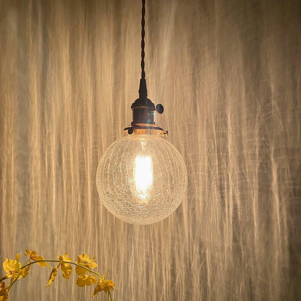 Artisanal crackle glass pendant light demonstrating fractured light scattering and prismatic luminescence effect through textured surface