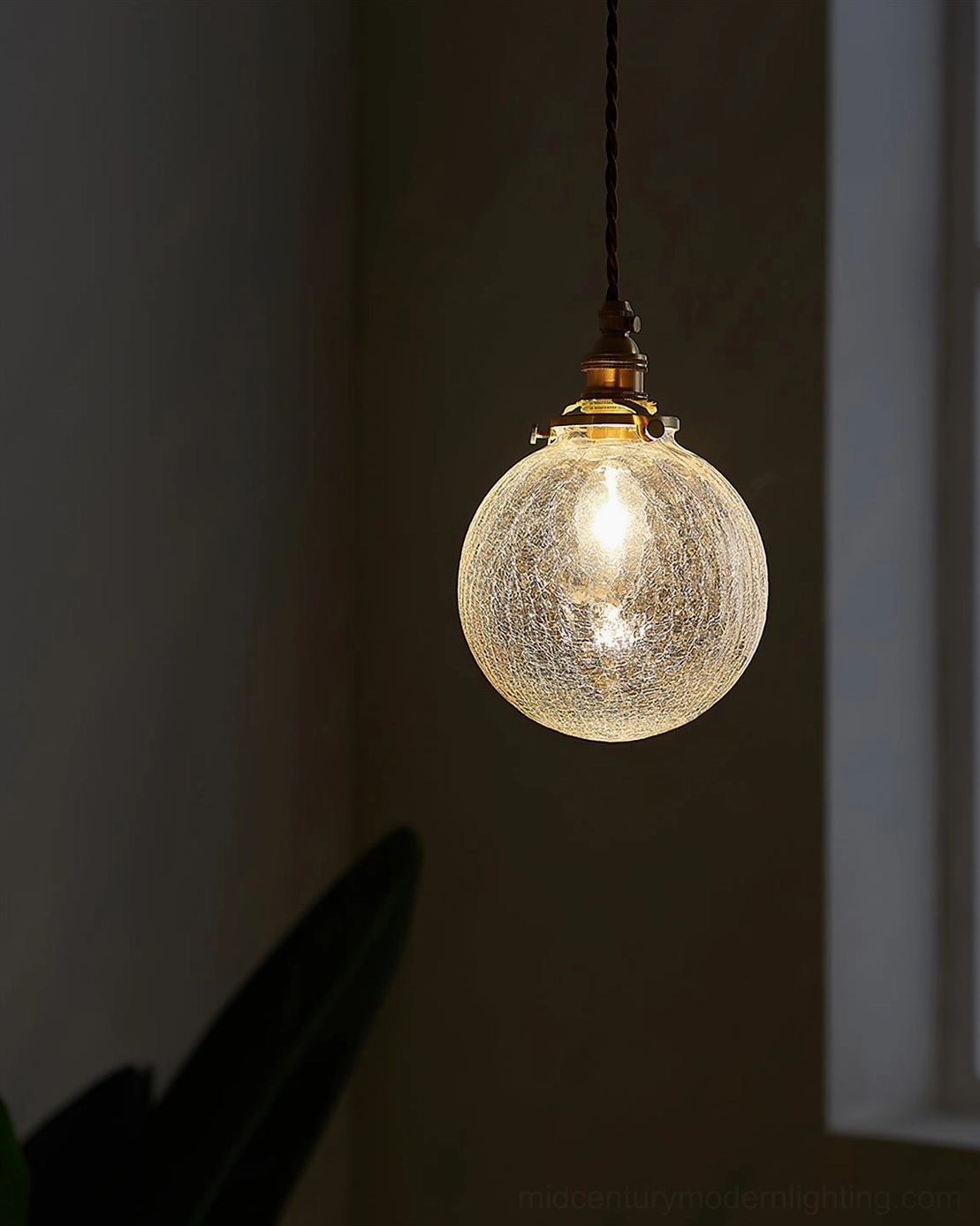 Crackle glass globe pendant light hanging close-up in dark indoor corner showing glowing fractured glass and brass top fitting