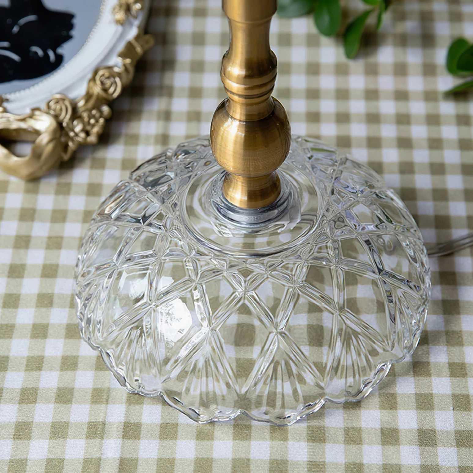 Close-up of carved crystal glass lamp base with brass metal stem on gingham tabletop