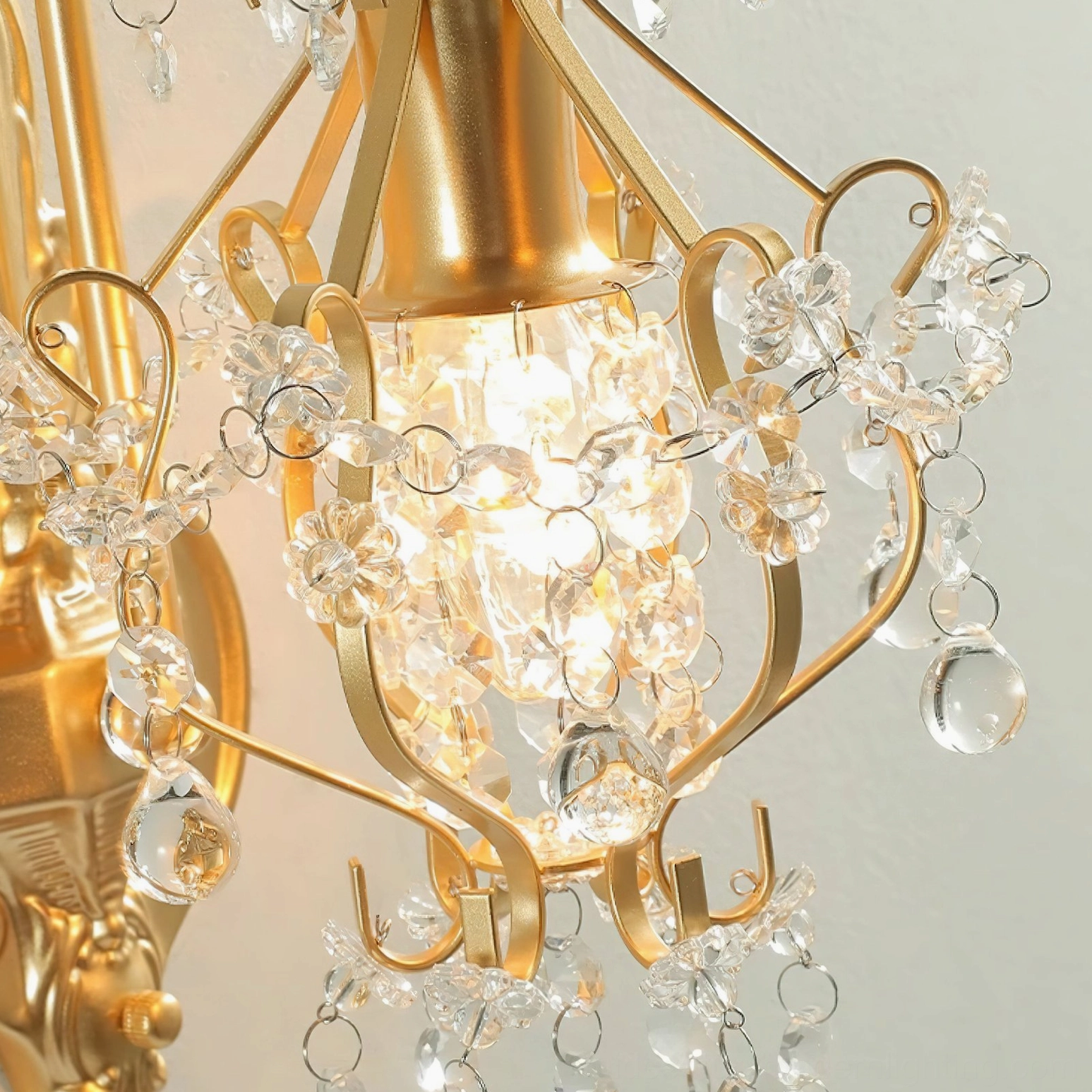 Close-up detail view of crystal wall sconce showing curved gold metal arms and hanging glass crystal elements