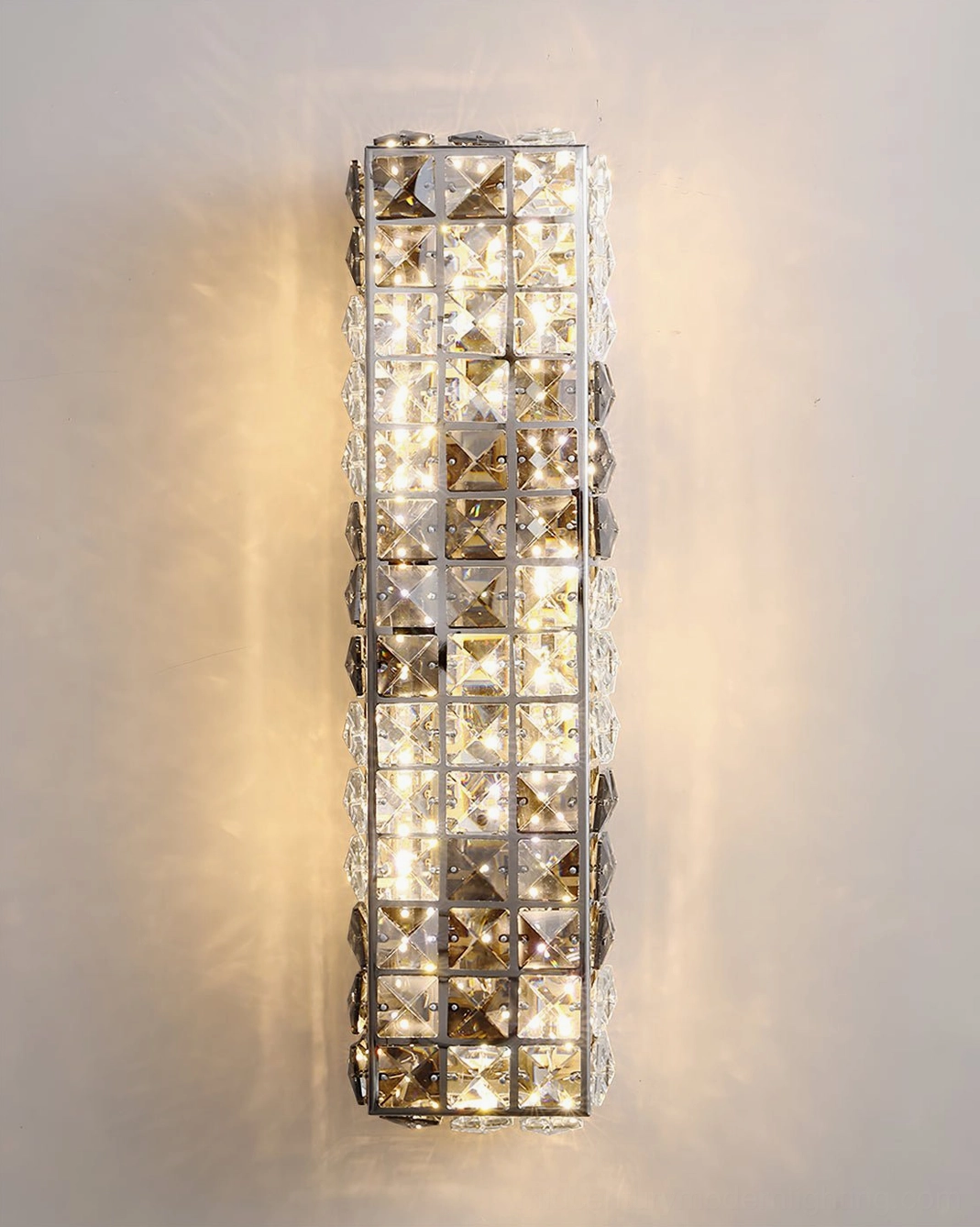 Close-up detail of faceted crystal wall lamp showing light refraction and warm LED glow against grey wall
