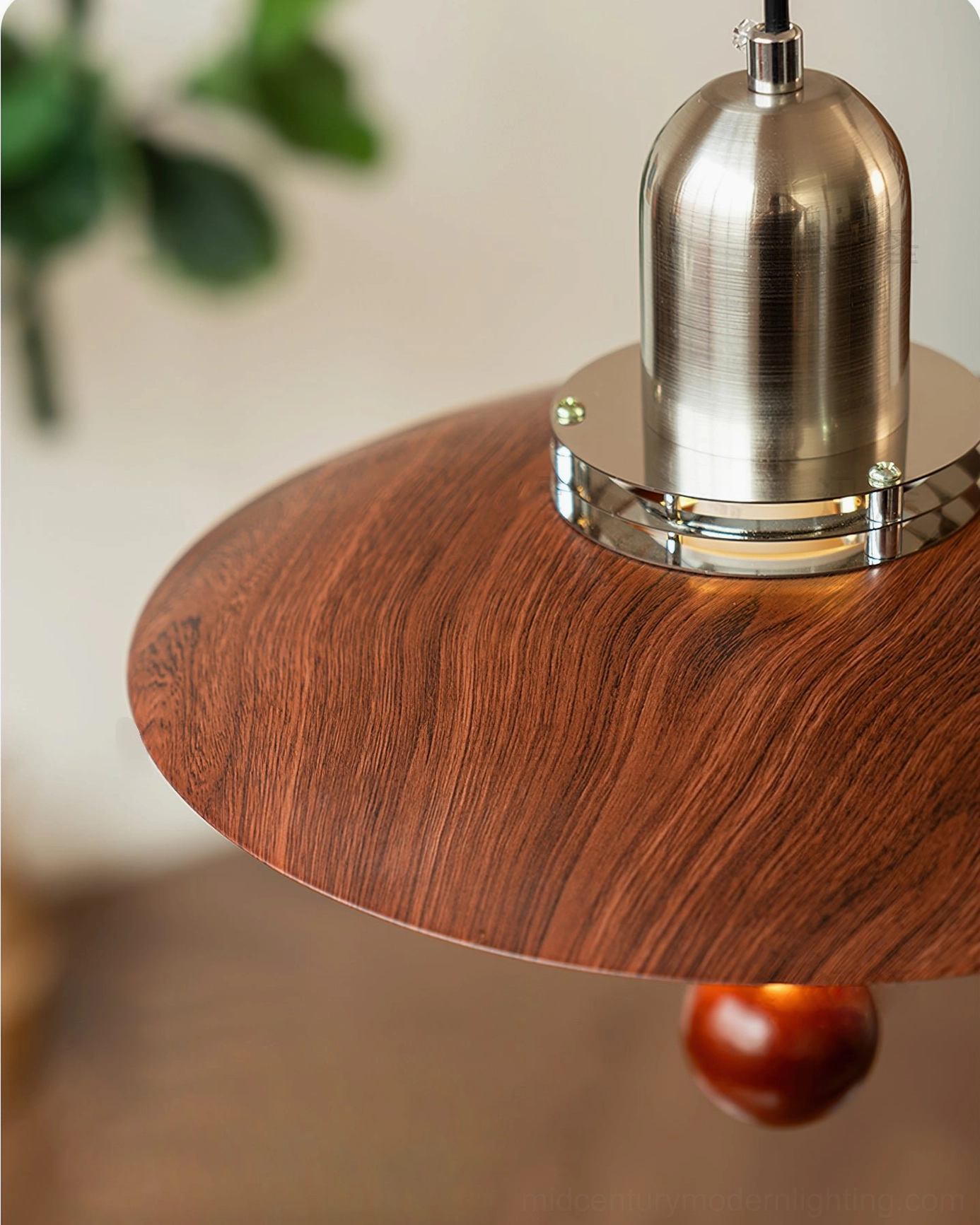 Detailed view of swing arm pendant light showing wood grain texture and metal joints with indoor plants and tabletop setting