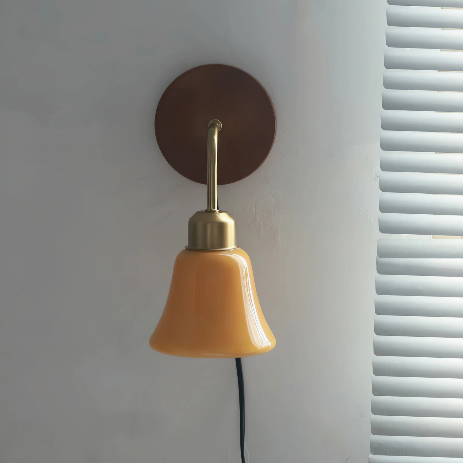 Daphne Pastel Plug-In Wall Sconce front-facing minimalist retro design with brass accent details and warm orange glass shade on white louver wall