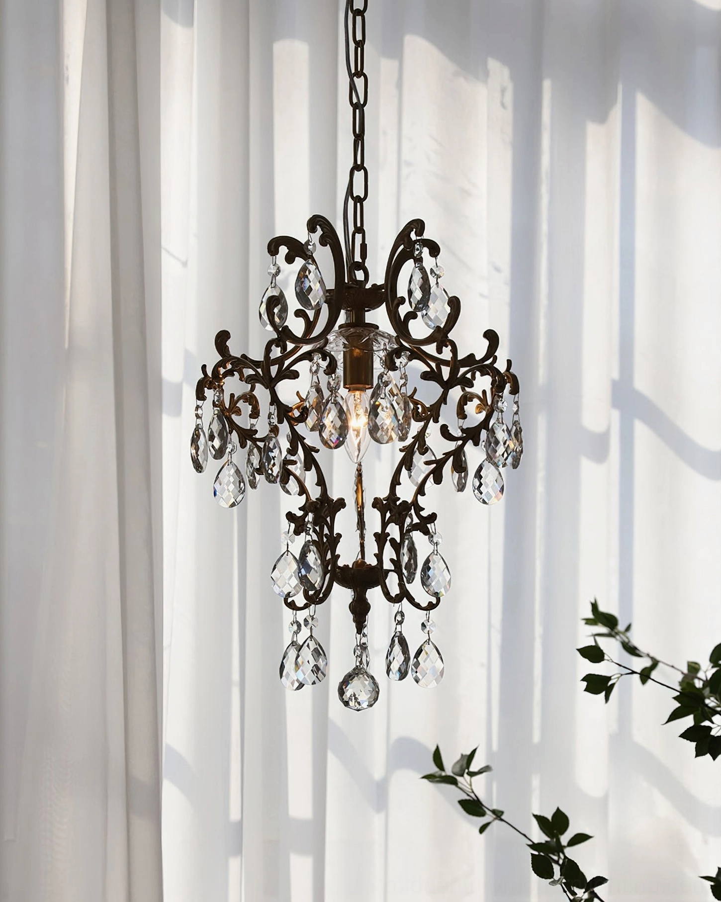 Dark bronze antique birdcage pendant with intricate scroll details and clear teardrop crystal decorations in soft lighting