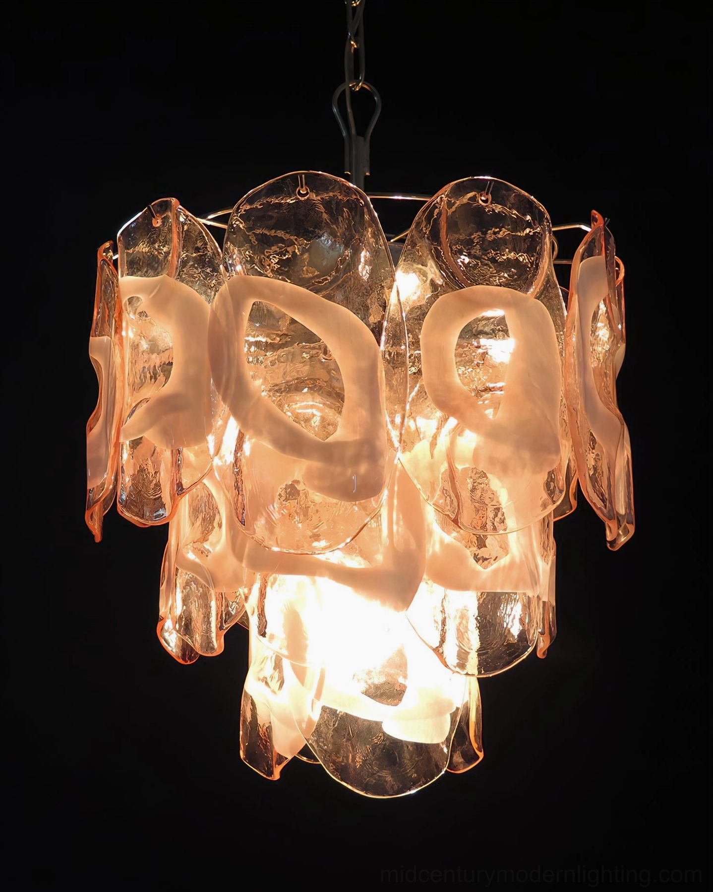 Delara pink glass chandelier at full illumination against black background, displaying warm glow and light diffusion through layered glass