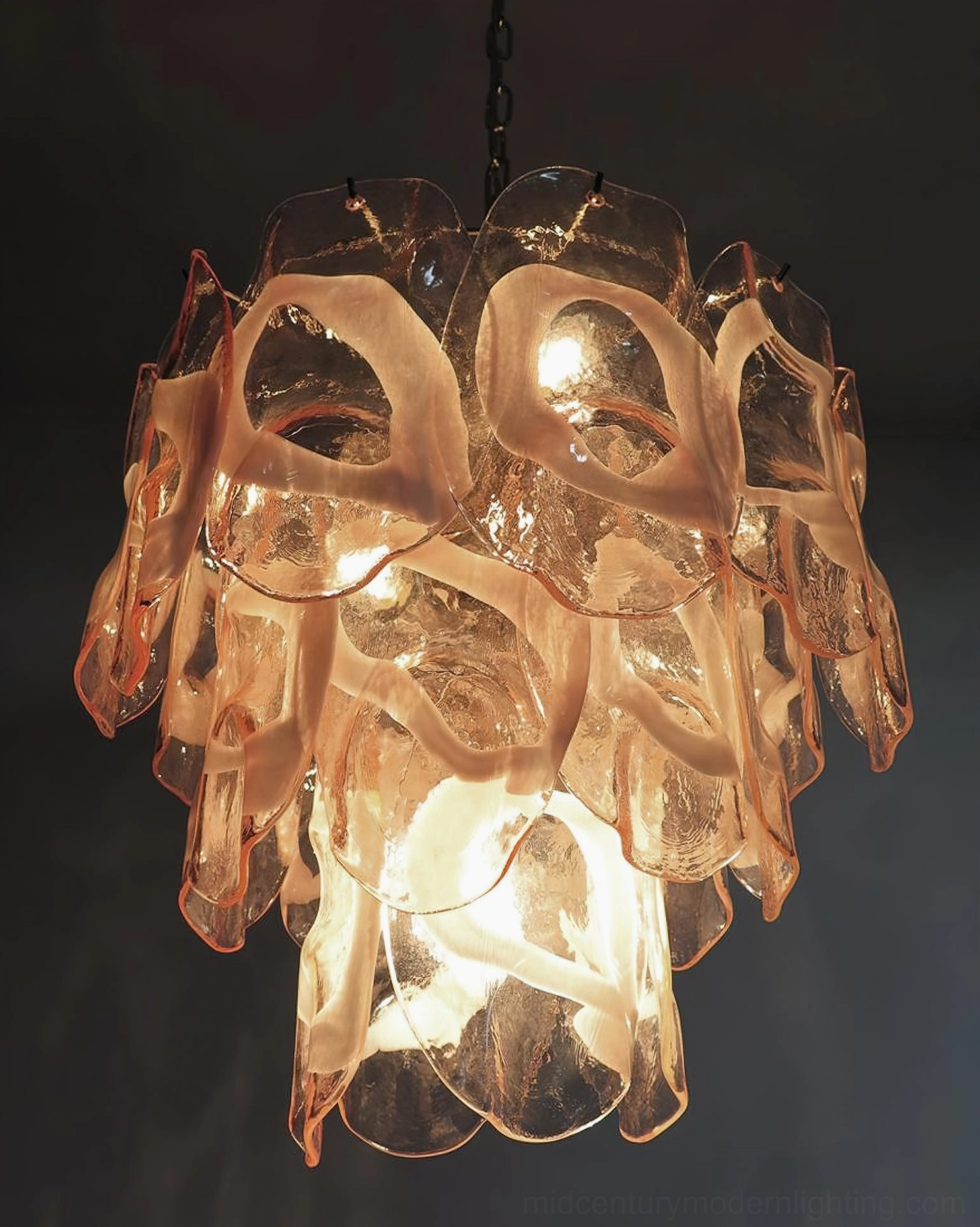 Fully lit Delara pink Murano glass chandelier creating warm amber glow, detailed close-up against black background