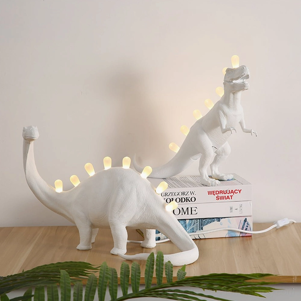 Two dinosaur table lamps styled on wooden desk with books, overhead flat composition