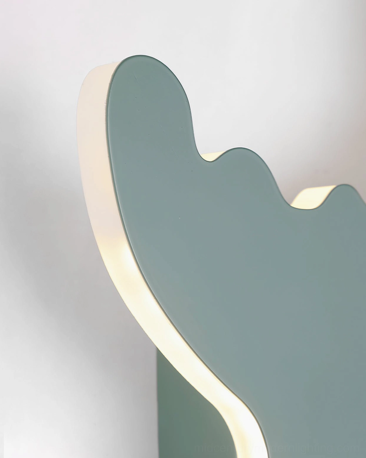 Close-up edge view of dinosaur wall lamp with glowing LED backlight and sage green matte surface finish
