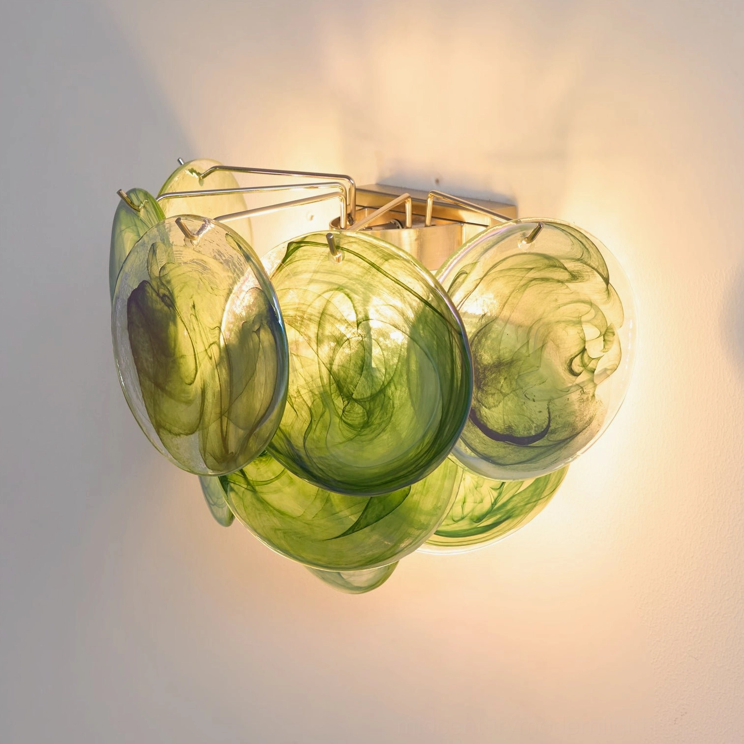 Illuminated green art glass disc wall lamp close-up, glowing warm light effect on handcrafted discs