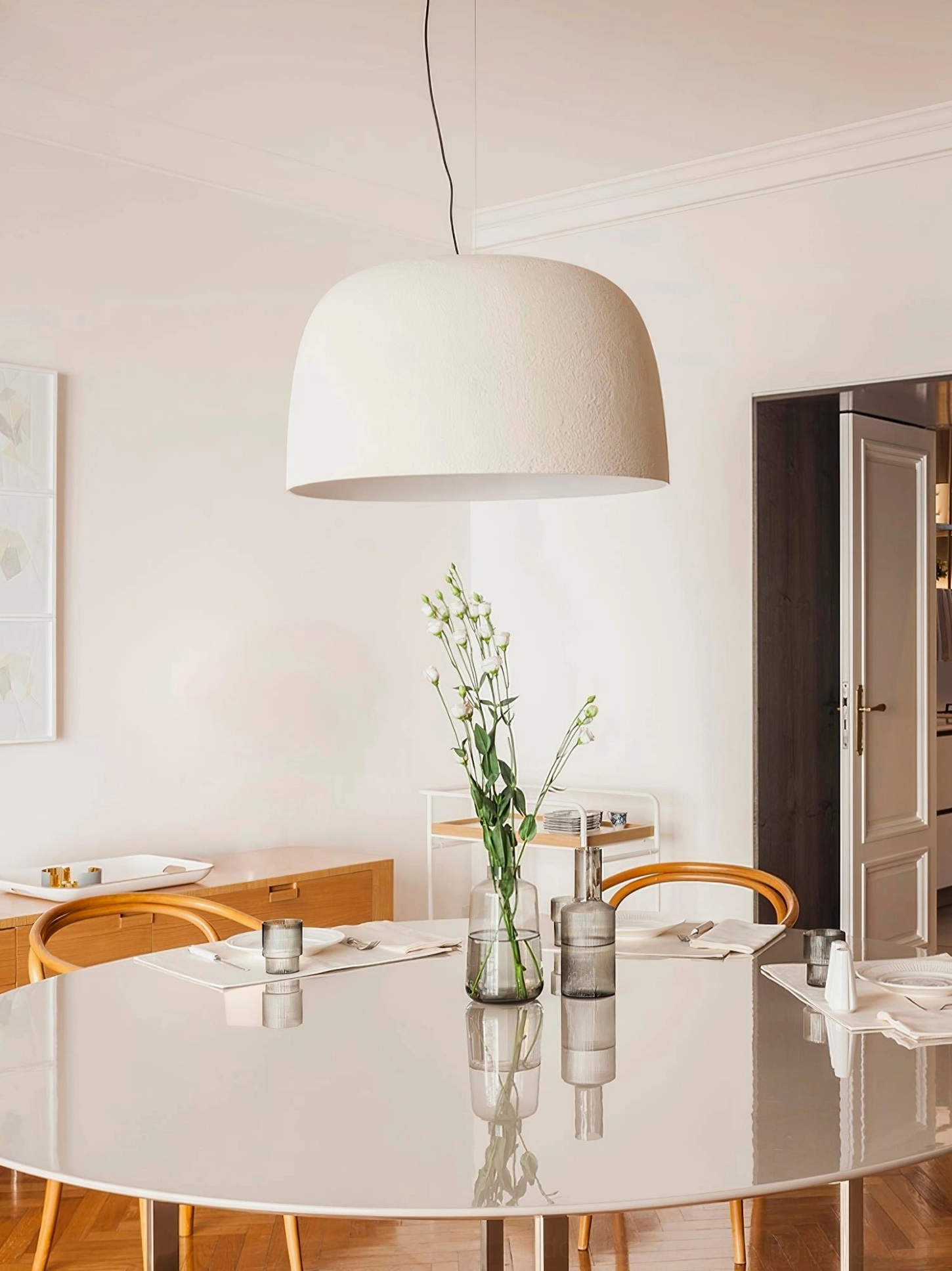 Off-white Djembe pendant lamp above dining table with round glass surface and floral centerpiece