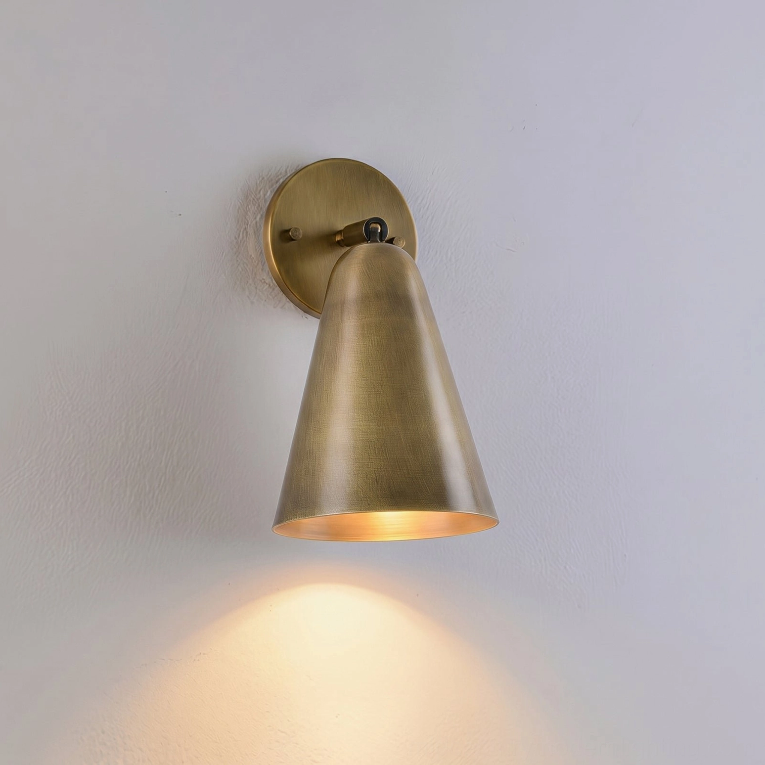 Donna brass sconce illuminated with warm downward lighting cone shade effect