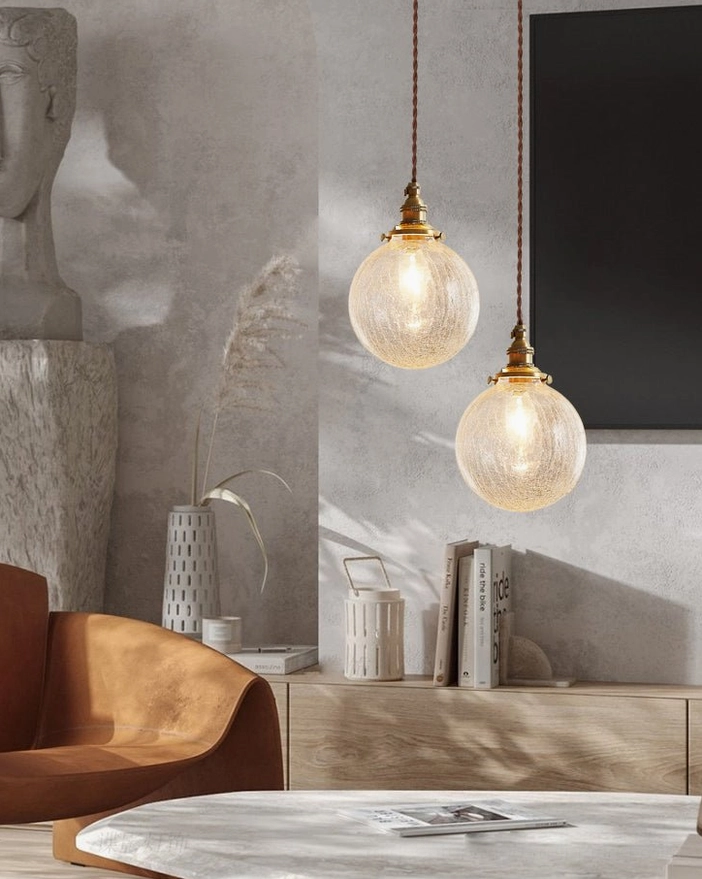 Dual crackle glass pendant lights installed above marble dining table in modern dining room with warm brass fixtures