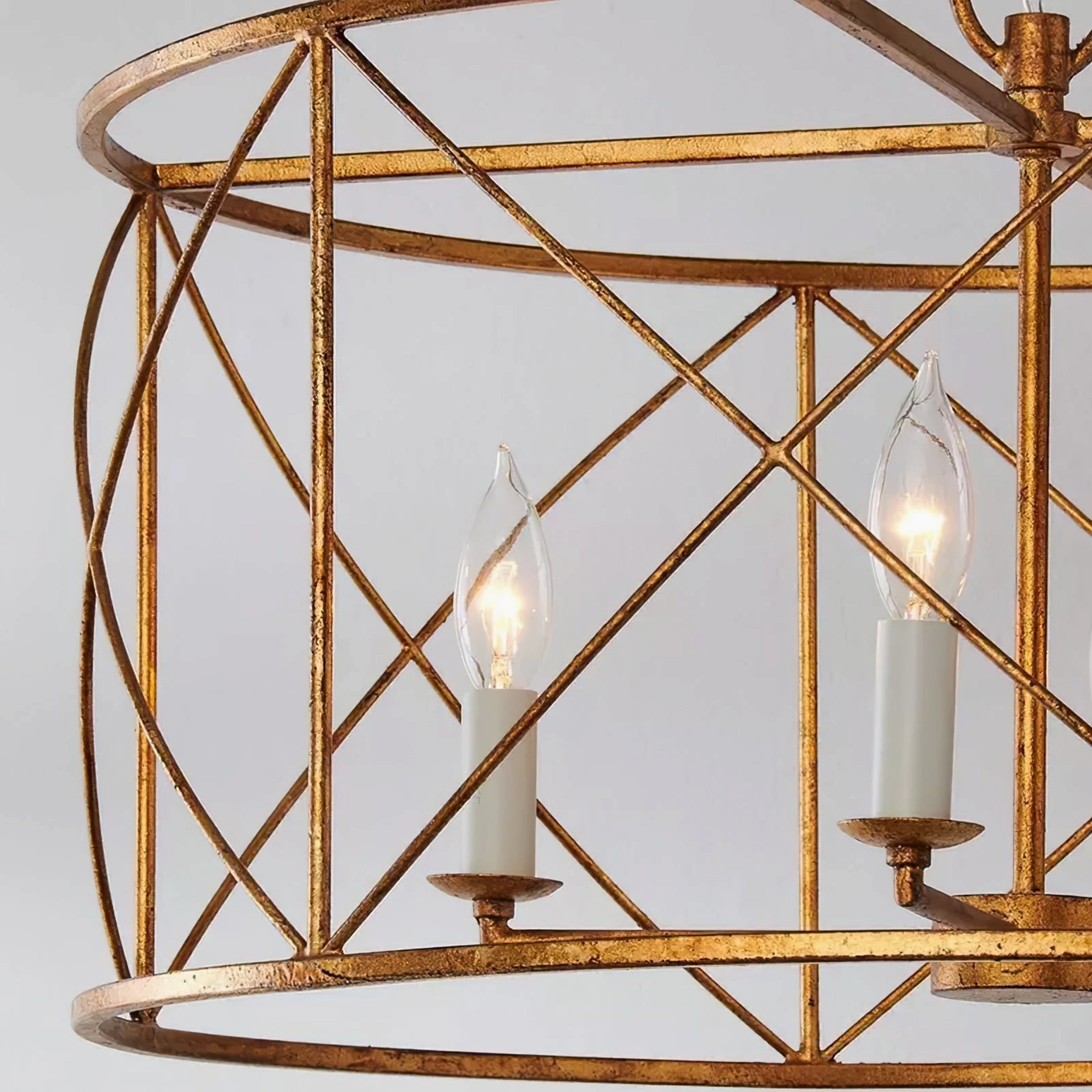 Close-up detail of lit candle-style E14 bulbs inside drum cage chandelier, showing cross-grid metal cage structure and warm glow