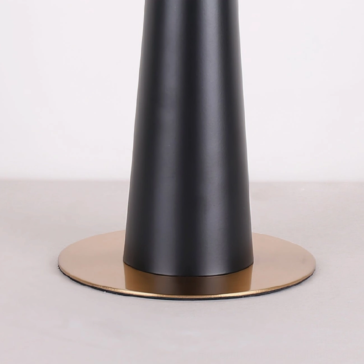 Close-up of matte black pole and polished gold metal base of drum table lamp