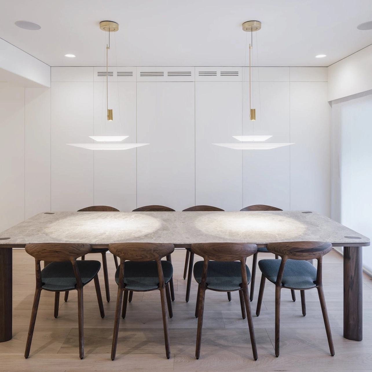Pair of Hover Disc chandeliers suspended above long luxury dining room table with white shade discs and brass hardware