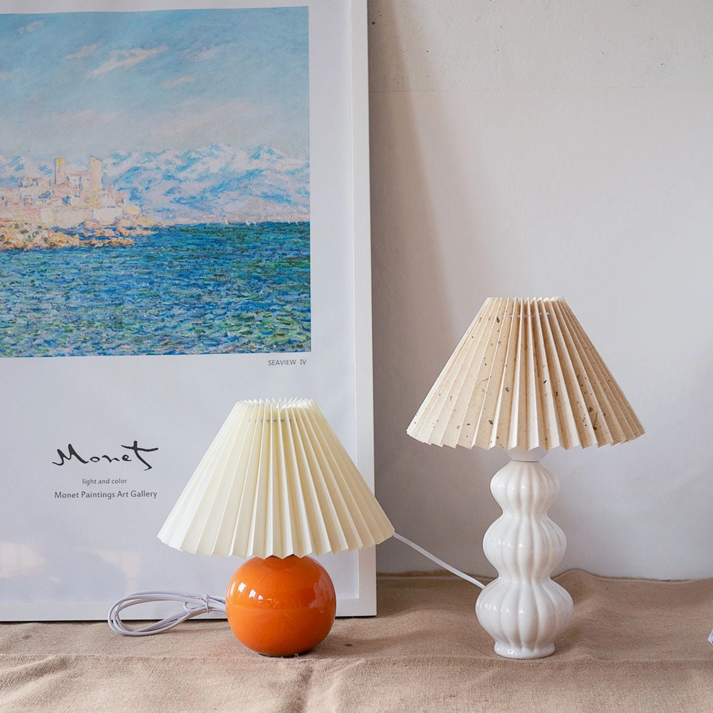 Two matching Luna pleated table lamps on tabletop, one white shade and one beige shade, identical white ceramic bases