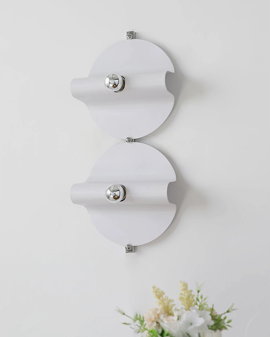 Two modern white and chrome wall sconces mounted symmetrically on white wall with floral decor