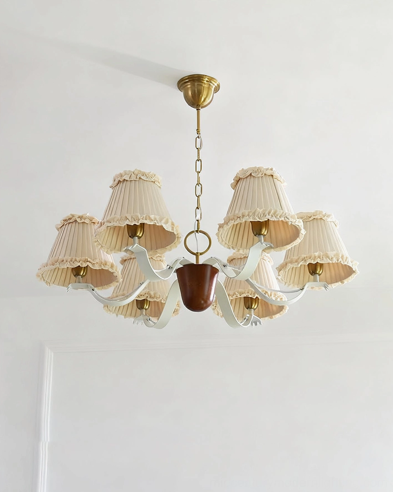 Multi-layer pleated off-white fabric chandelier shades with brass chain and dark wood central detail, overhead view