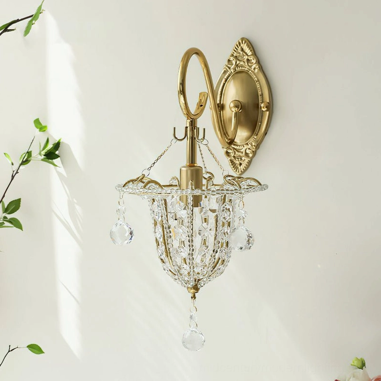 Elegant luxury Eilers brass crystal wall sconce with polished gold finish and crystal bead trim mounted on sunlit white wall with delicate green branches