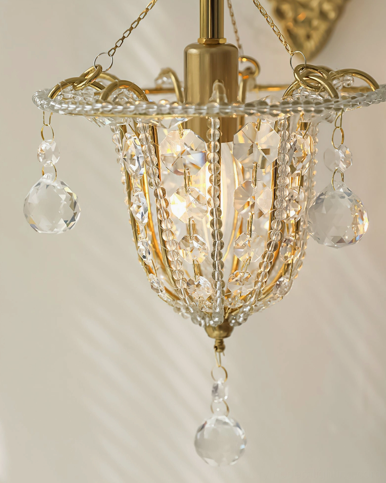 Close-up illuminated view of Eilers crystal wall sconce showing glowing inner lamp and clear crystal drops catching light, romantic vintage luxury design