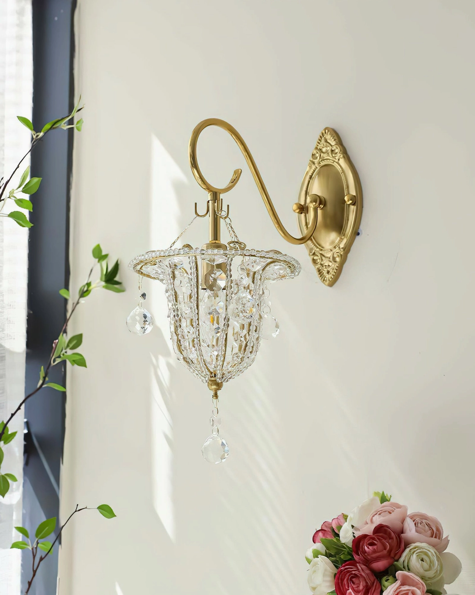 Eilers crystal wall light installed indoors beside window with fresh flower bouquet, showcasing romantic vintage design with curved brass arm and cascading crystal accents