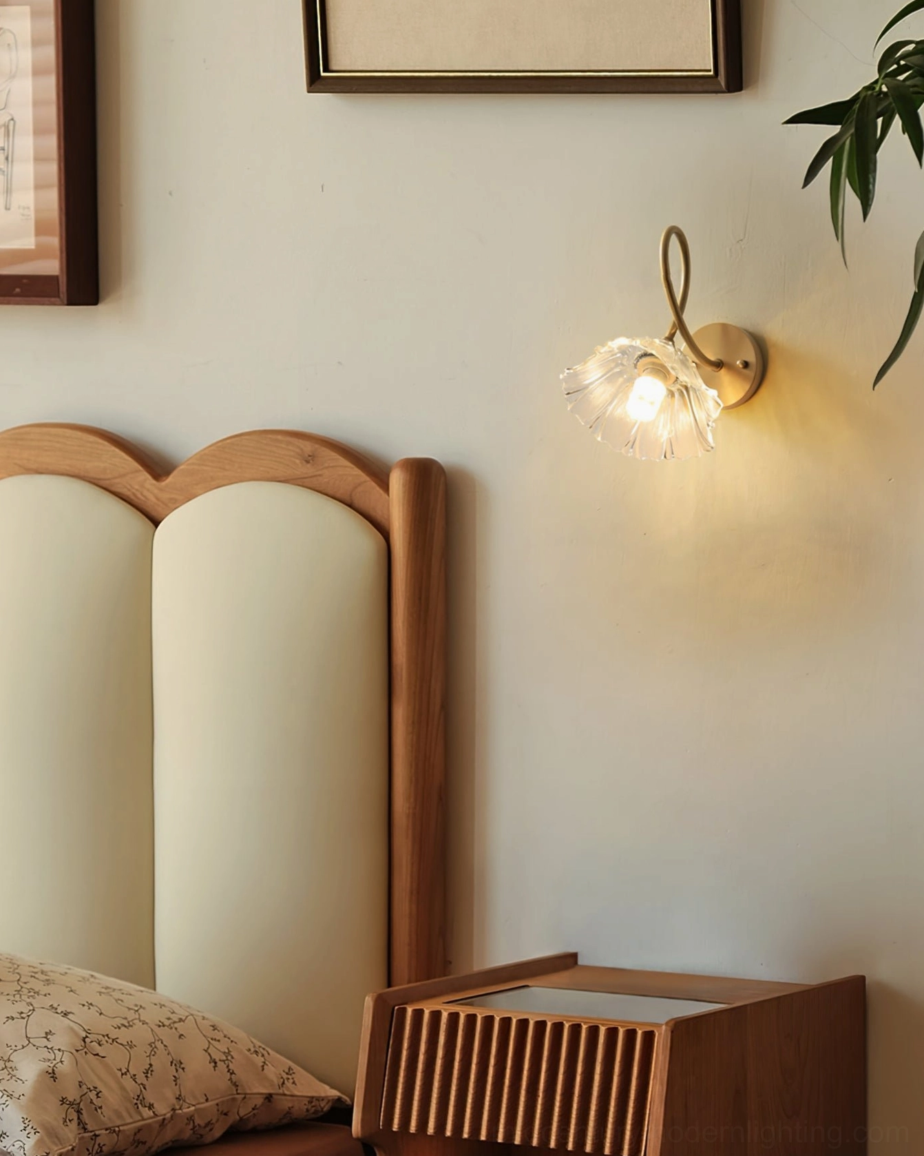 Ercole wall sconce glowing beside upholstered headboard creating intimate bedroom lighting