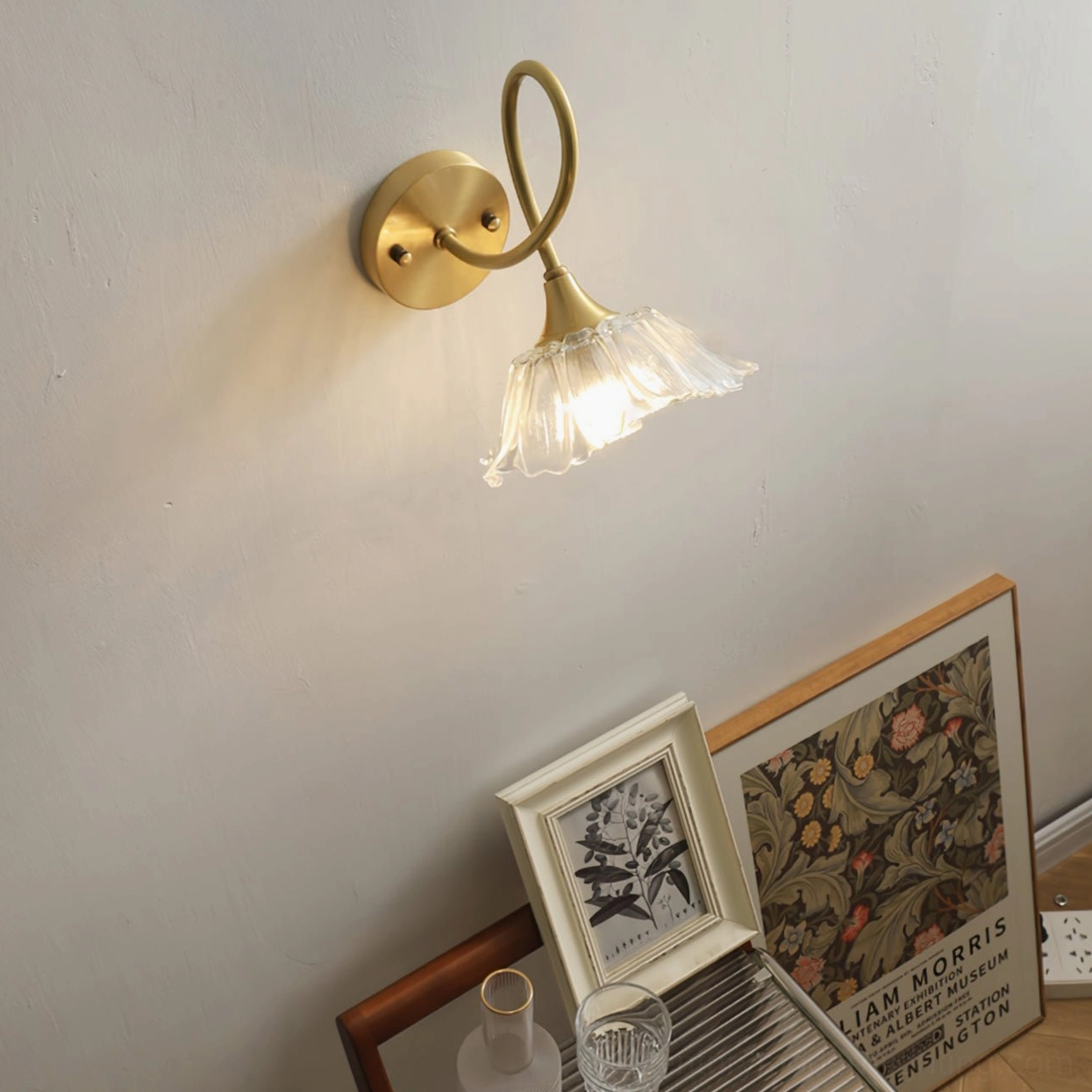 Ercole wall sconce illuminated in corner space with framed art prints and twisted gold arm