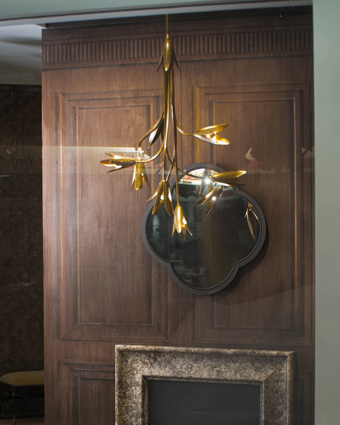 Evadne brass tulip chandelier glowing above quatrefoil mirror in classic vintage interior with dark wood panels