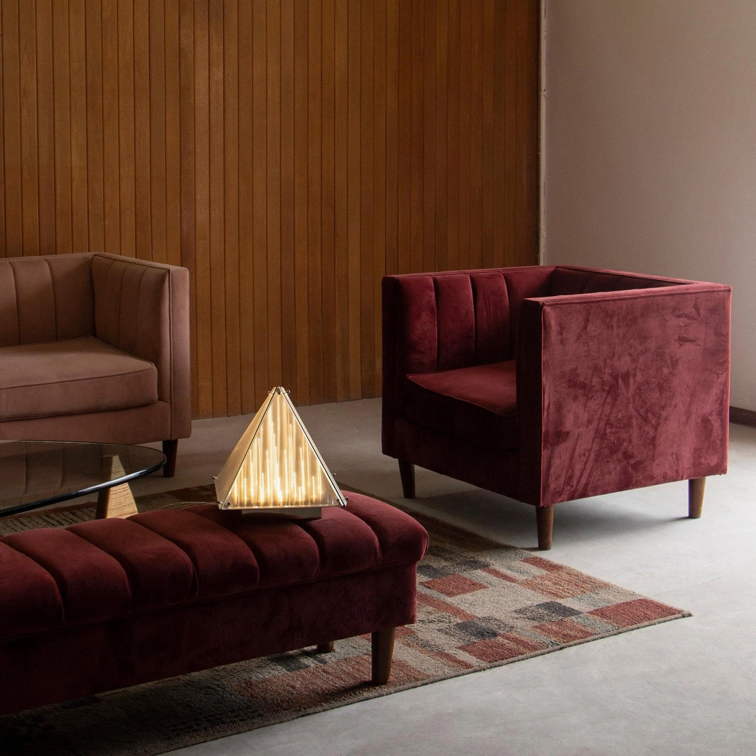 Fragment pyramid table lamp on velvet ottoman in mid-century modern lounge with wood paneling