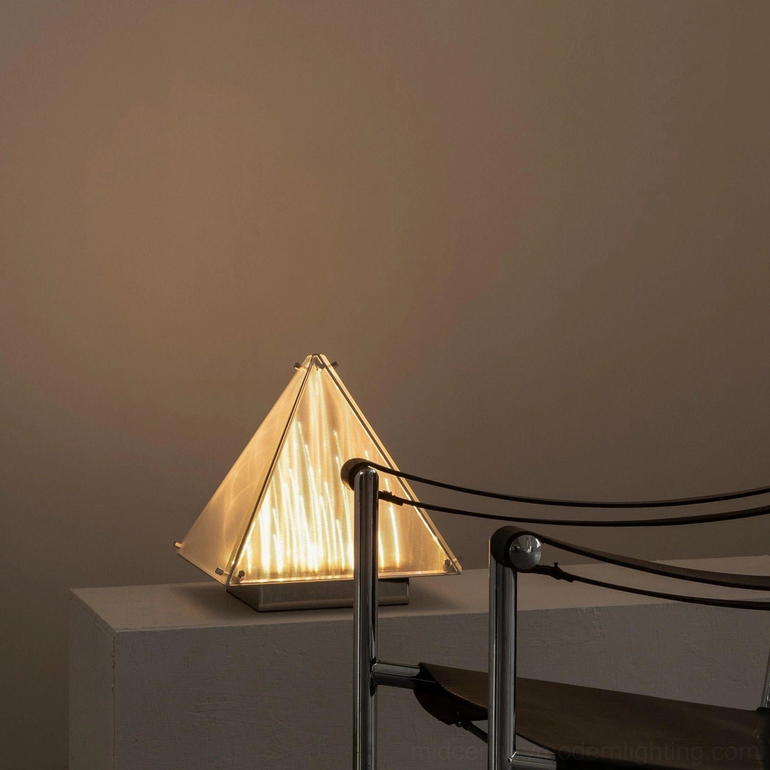 Minimalist pyramid shaped lamp on concrete console table with metal chair in contemporary space