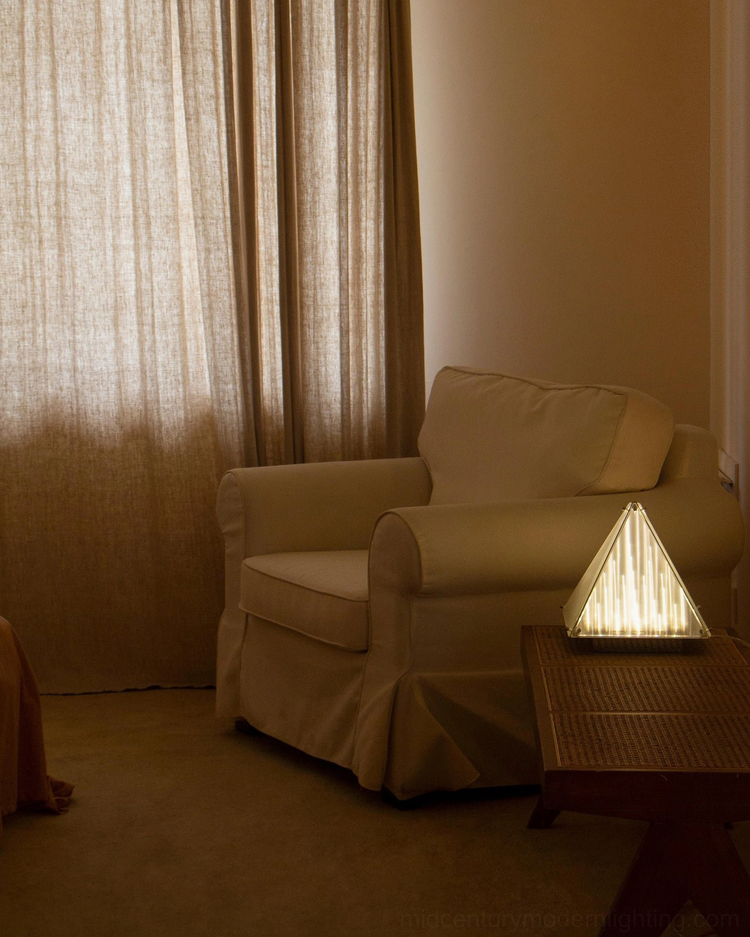 Pyramid shaped lamp in cozy reading corner with sheer curtain backdrop and warm ambient glow
