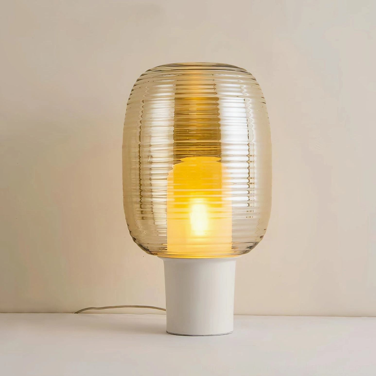 Ghia cognac amber ribbed glass table lamp with white base lit interior view against soft wall backdrop