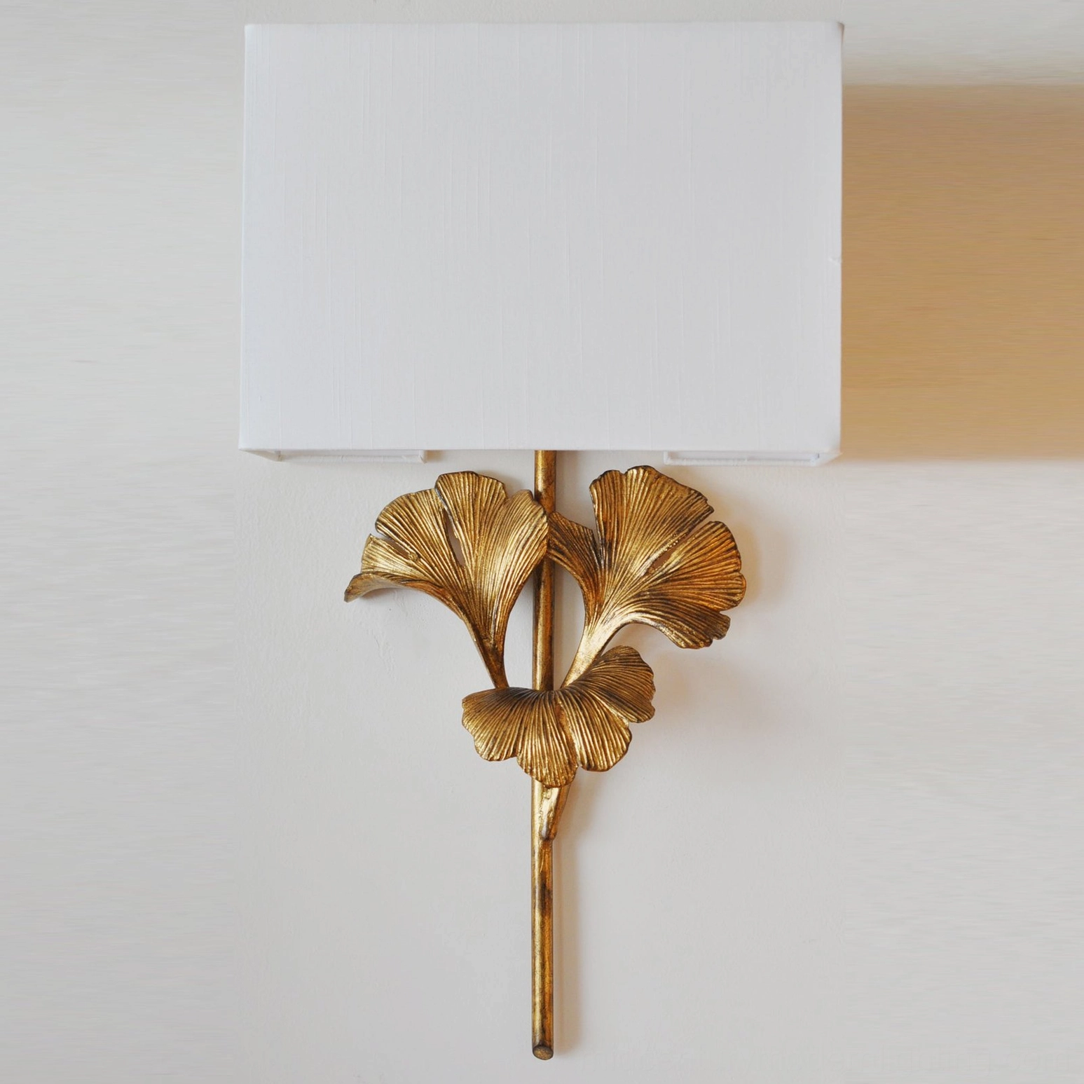 Close-up detail of gingko wall lamp showing polished brass leaf frame and rectangular fabric shade