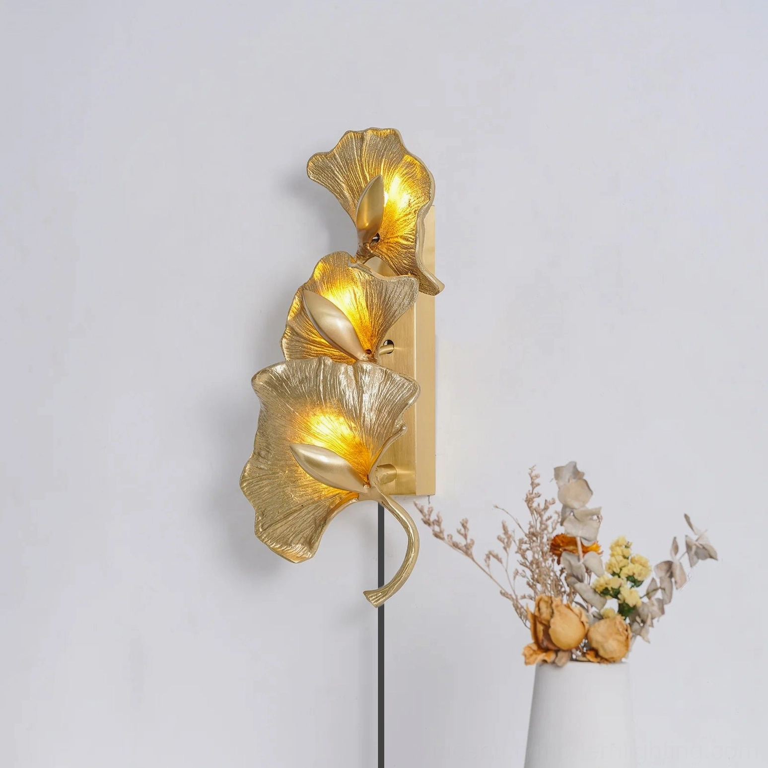 Golden ginkgo leaf wall lamp glowing with warm light in scandinavian style room with botanical decor