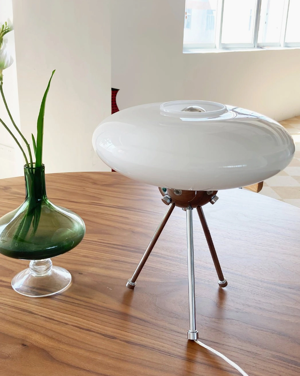 Glass UFO lamp paired with green flower vase on wooden table, dining room arrangement