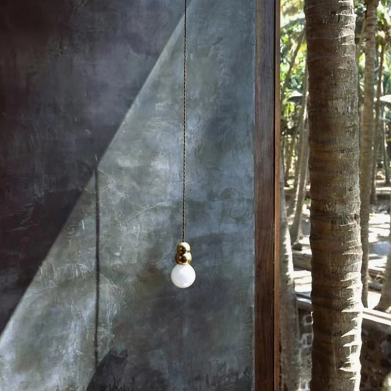 Gold ball wall sconce outdoor installation, textured concrete wall with palm trees, contemporary lighting