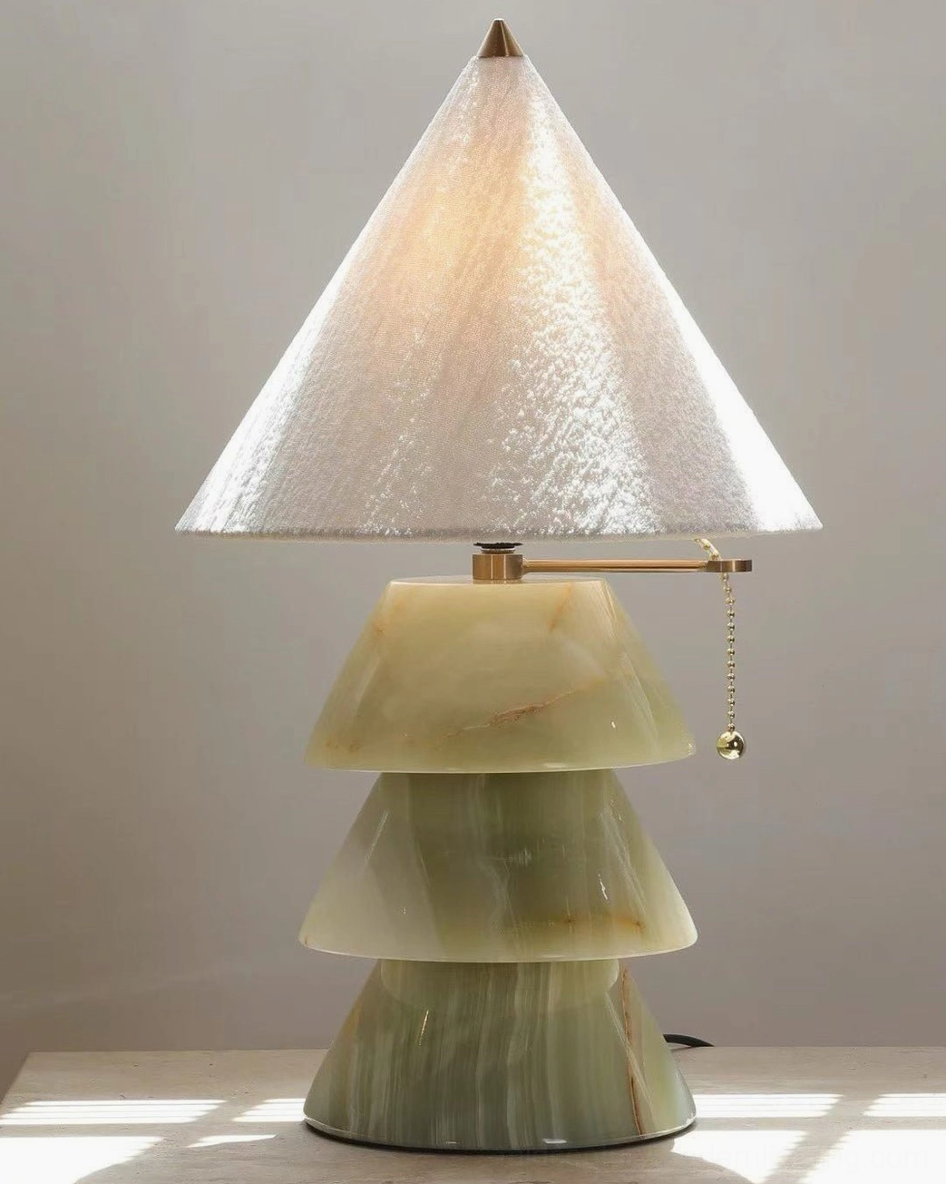 Green marble pyramid lamp base with brass chain switch detail on luxury marble tabletop