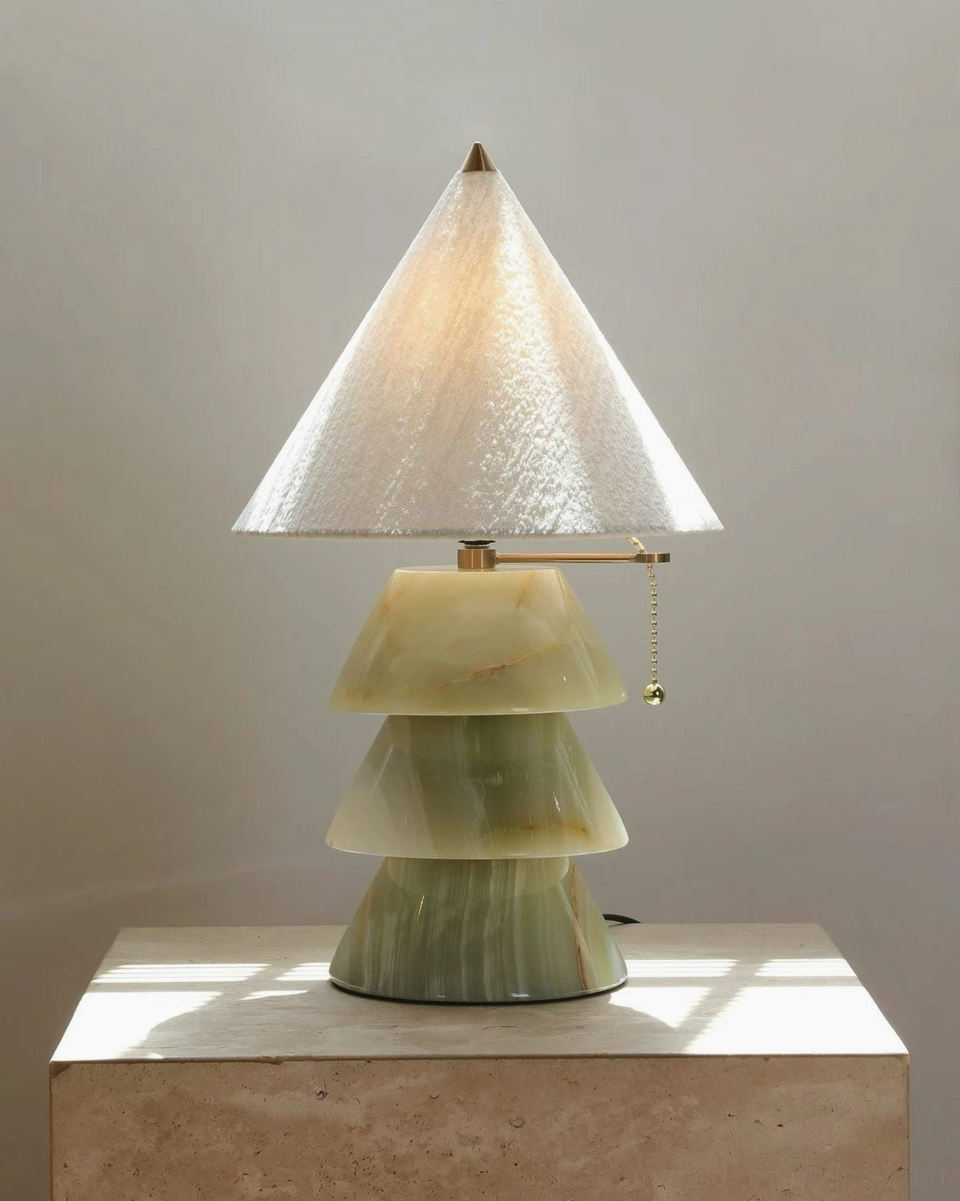 Gradient green jade pyramid marble lamp with textured fabric shade and brass hardware on sunlit stone surface