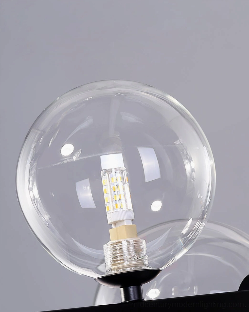 Close-up macro view of hand-blown clear glass bubble orb with integrated LED lamp bead on grey studio background