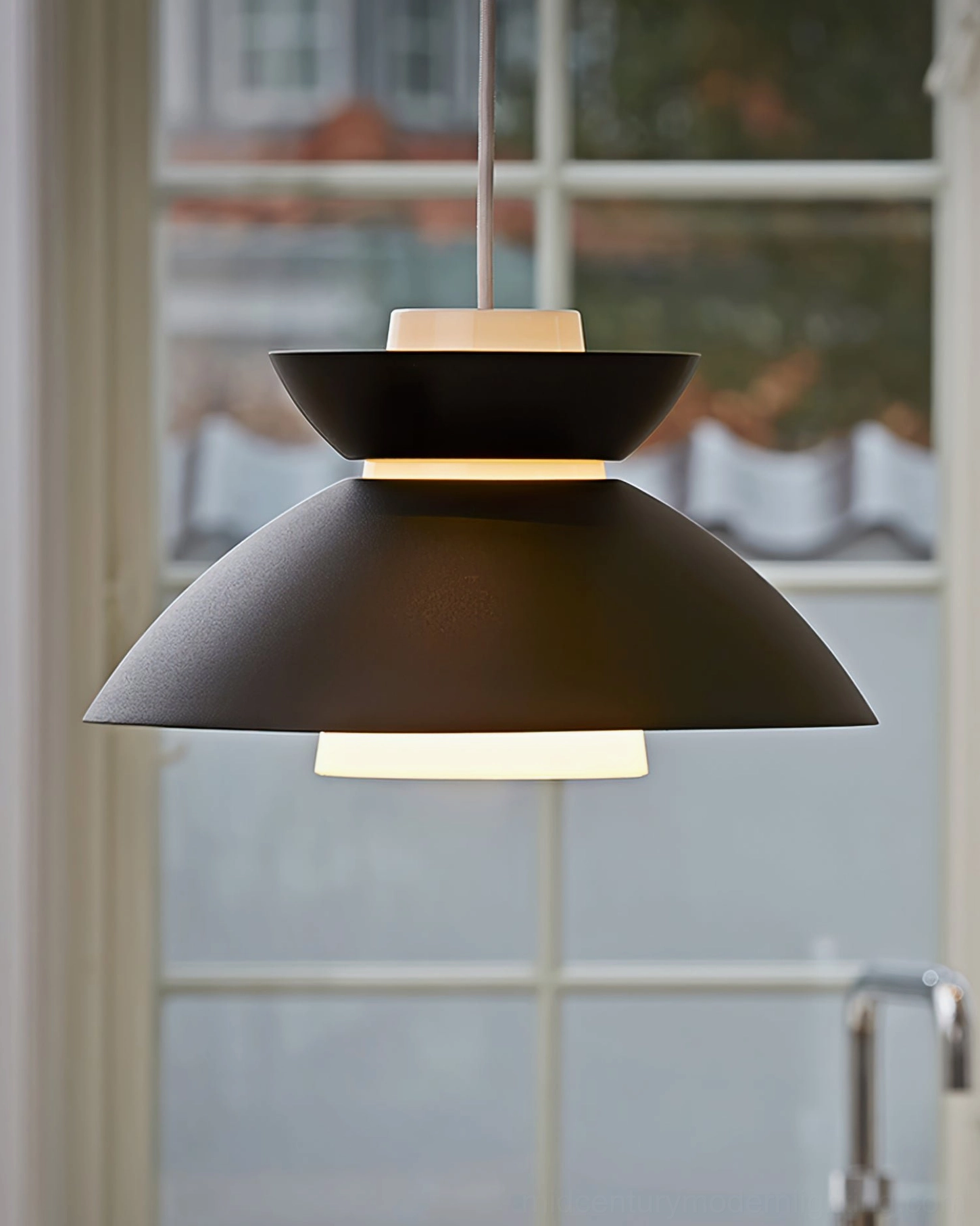 Hannes pendant lamp illuminated above kitchen window, side view showing warm ambient glow and layered silhouette