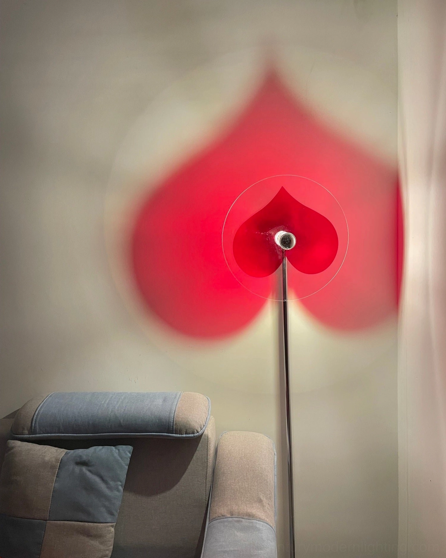 Heart projection floor lamp with pointed-top red heart shadow displayed in living room with grey sofa in background