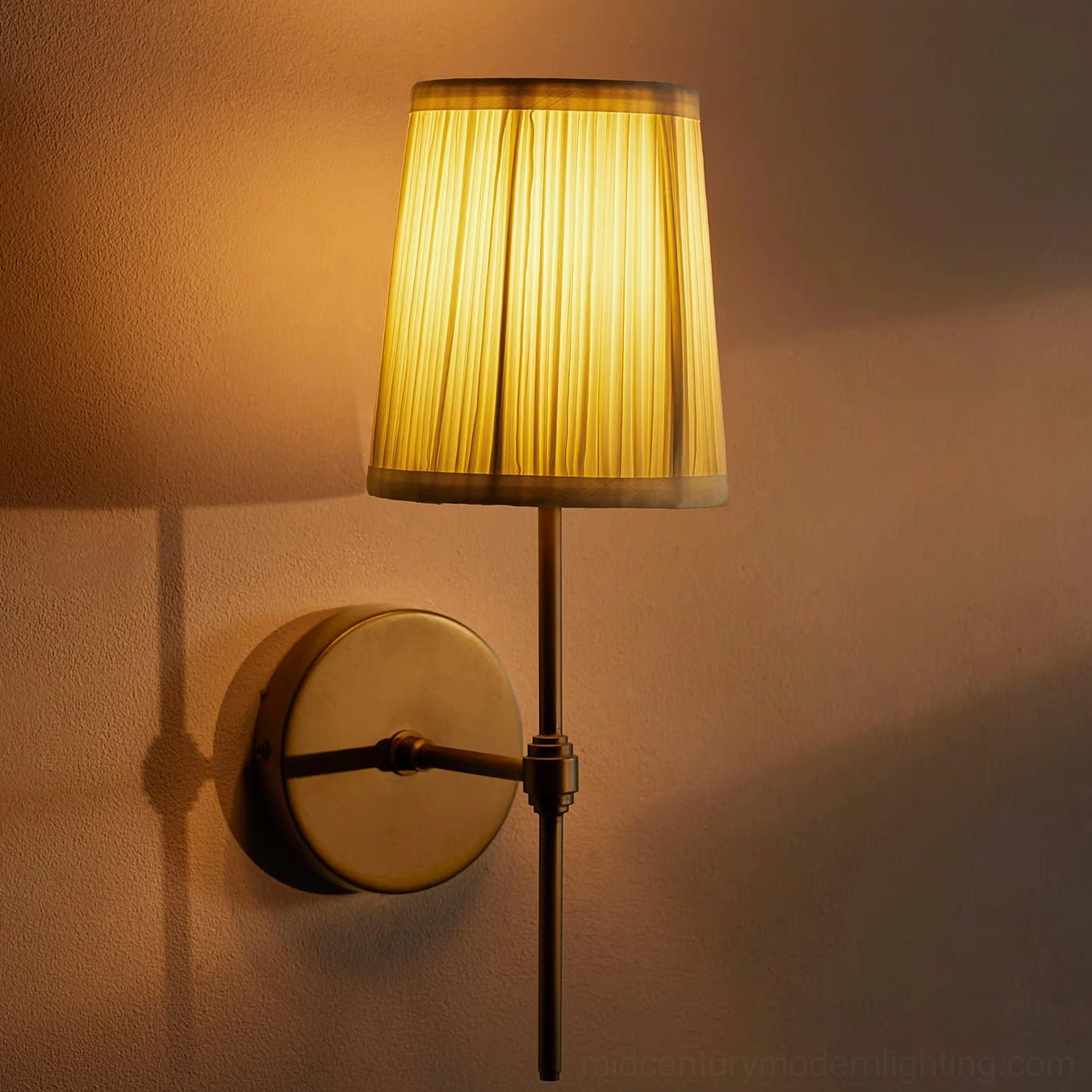 Lit Henley wall sconce viewed from side angle with warm shadow cast on wall showing brass base and diffused glow